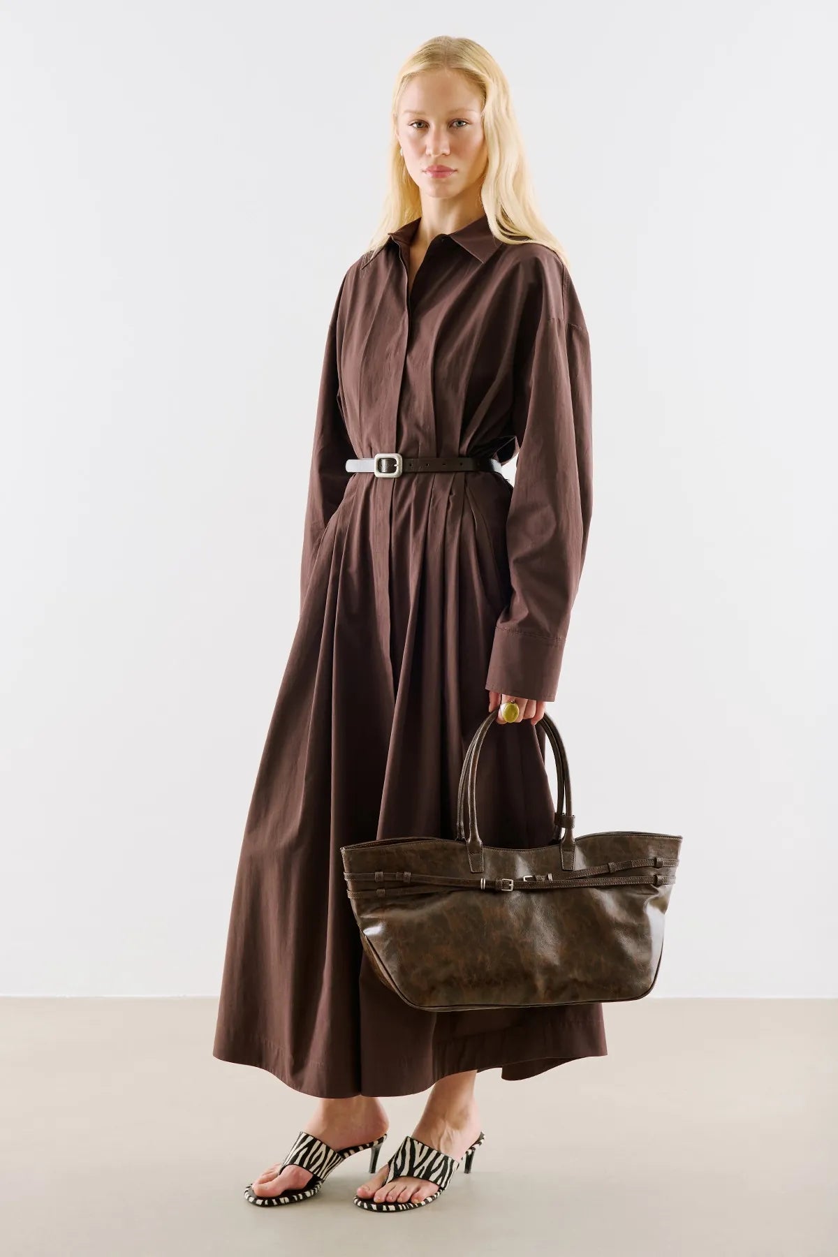 A long chocolate-brown shirt dress, belted at the waist, with a brown leather tote.