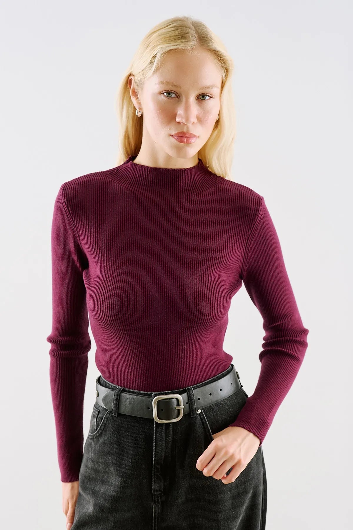 A claret ribbed knit with a high neck, worn with a black leather belt.