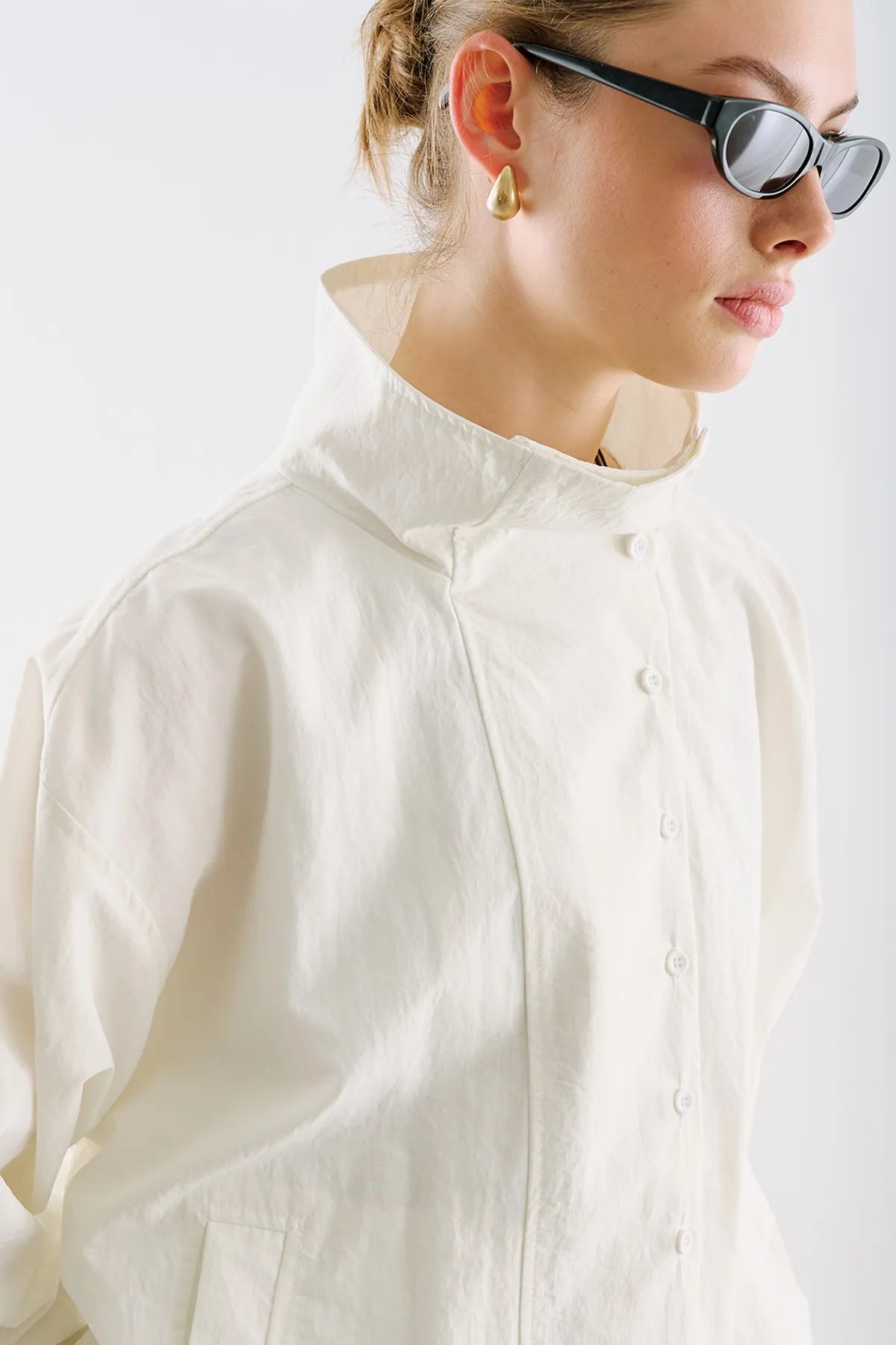A close detail of a cream shirt with a high, buttoned collar.