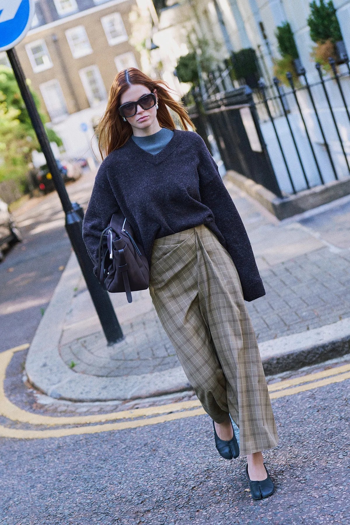 A navy knit worn with grey plaid trousers on a London street corner.