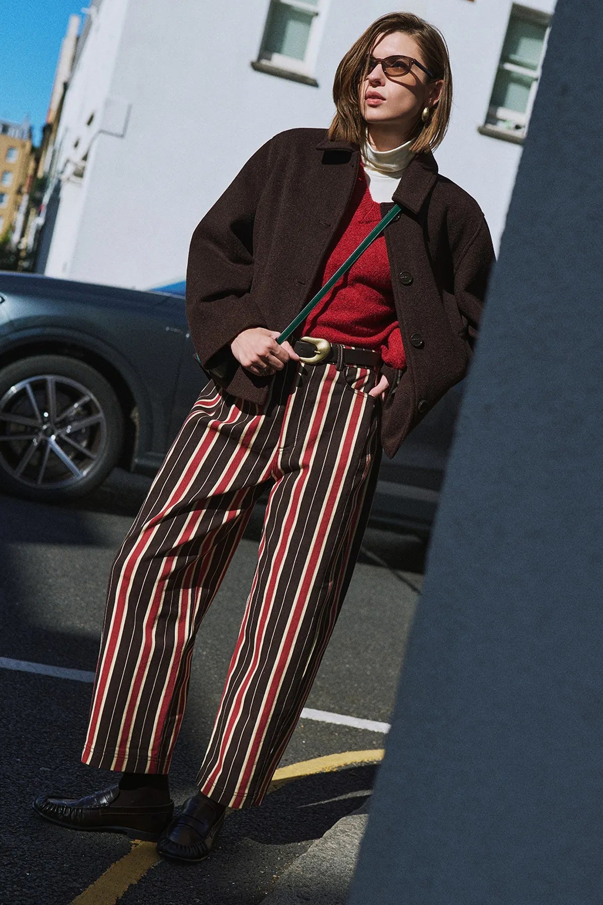 A brown jacket over a red top with striped trousers, in the wind.